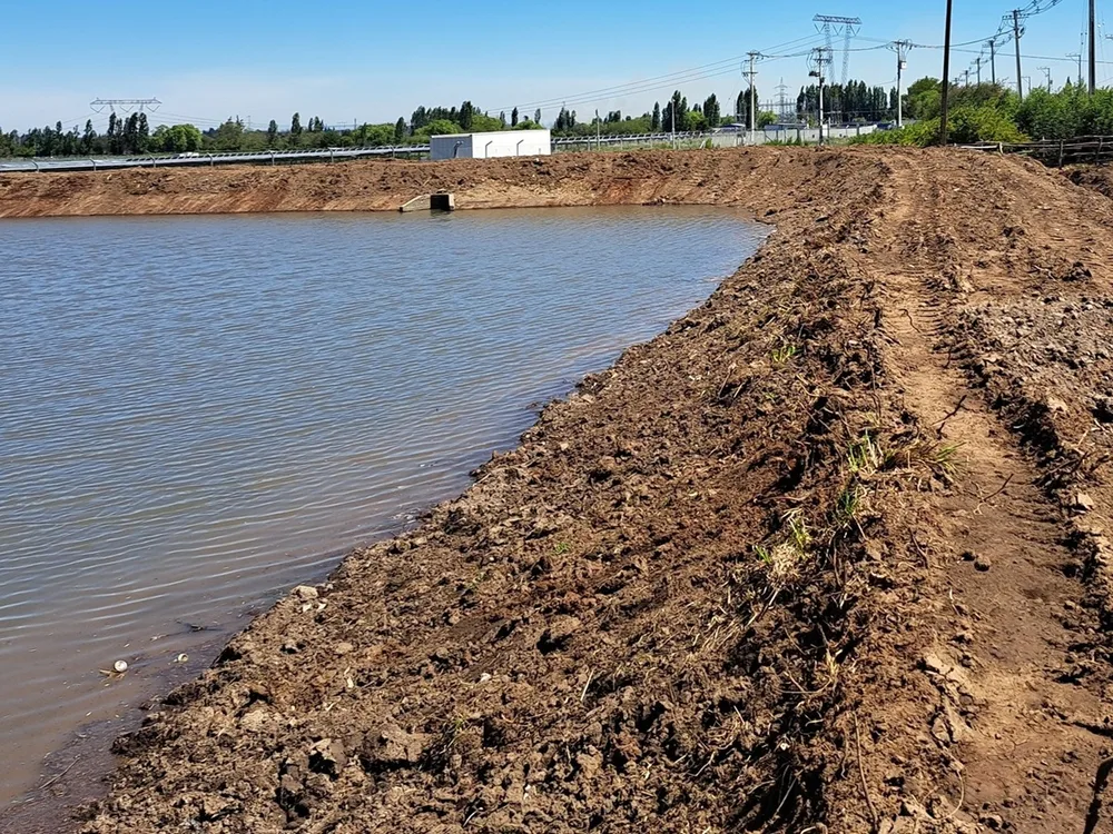 Sector con movimientos de tierra junto a un cuerpo de agua e infraestructura en el entorno